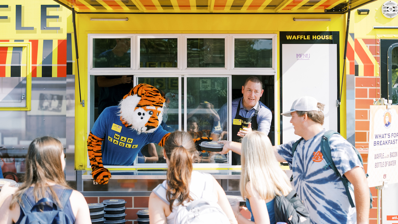 Aubie and Dr. Woodard serve waffles to students out of a Waffle House food truck during Waffles with Woodard