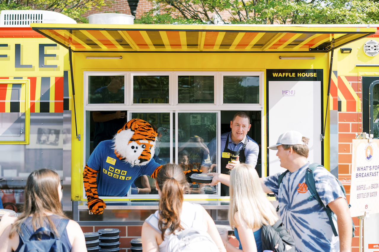 Aubie and Dr. Woodard serve waffles to students out of a Waffle House food truck during Waffles with Woodard