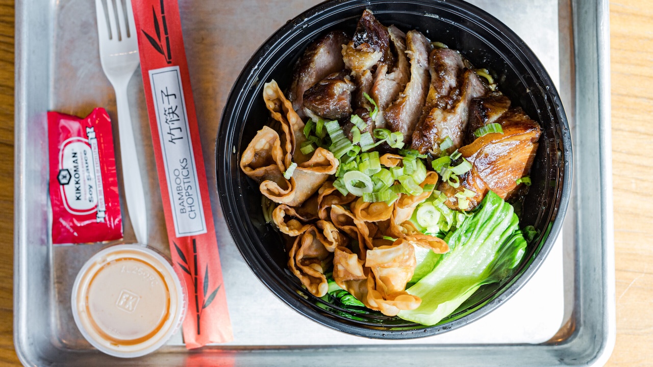 a tray with a noodle bowl from khoodles containing sliced meat, rangoons, bok choi and chives