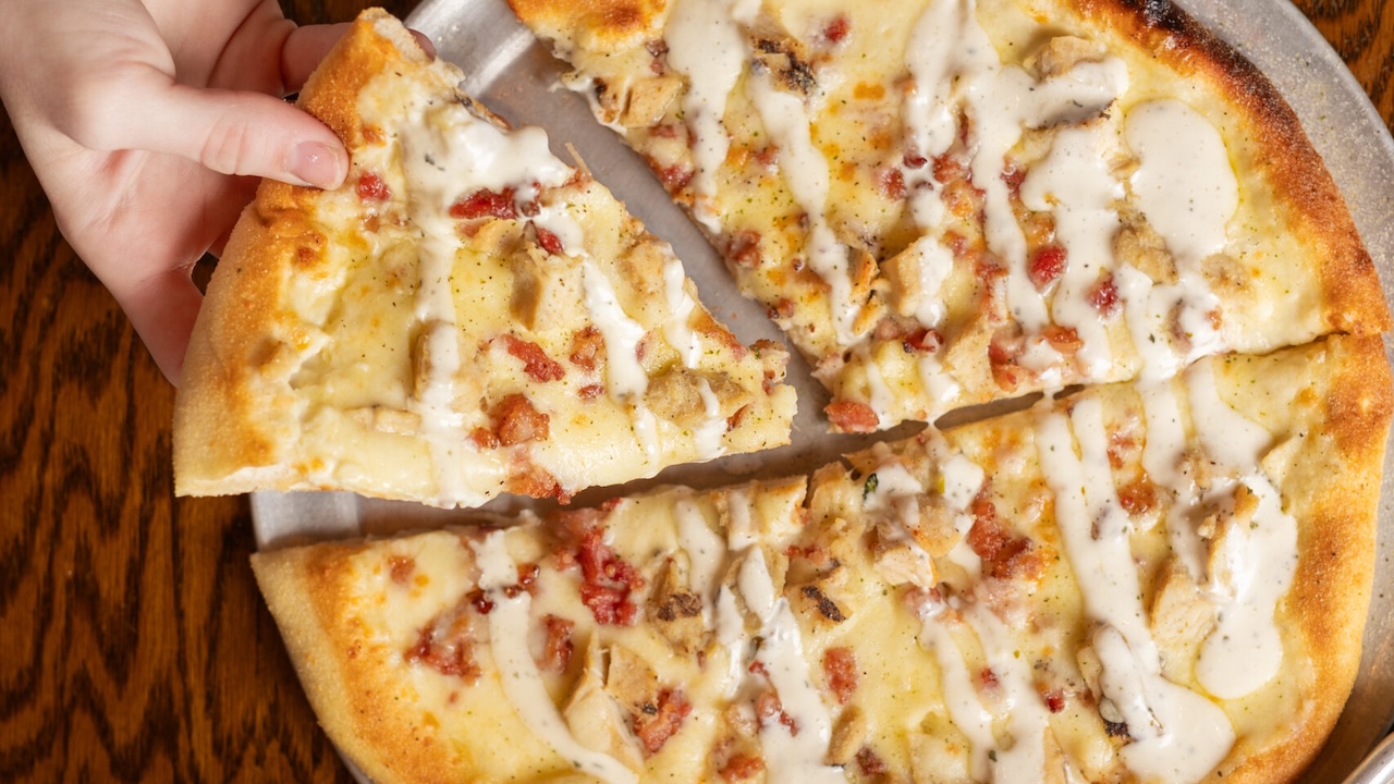 a hand taking a slice of chicken bacon ranch pizza