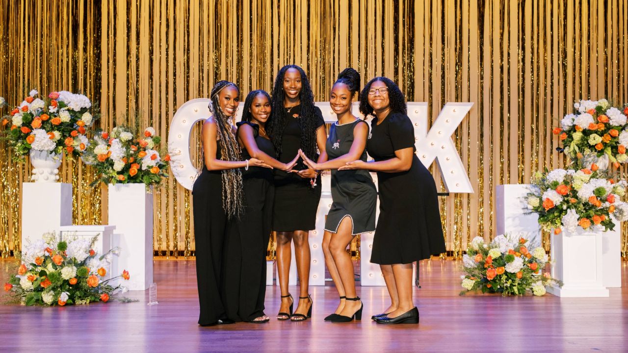 Women on stage holding up the hand sign of Delta Sigma Theta Sorority, Inc.