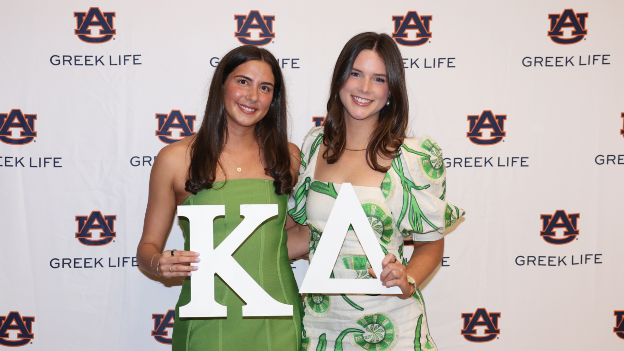 Two women smiling at the camera holding a wooden Kappa and Delta