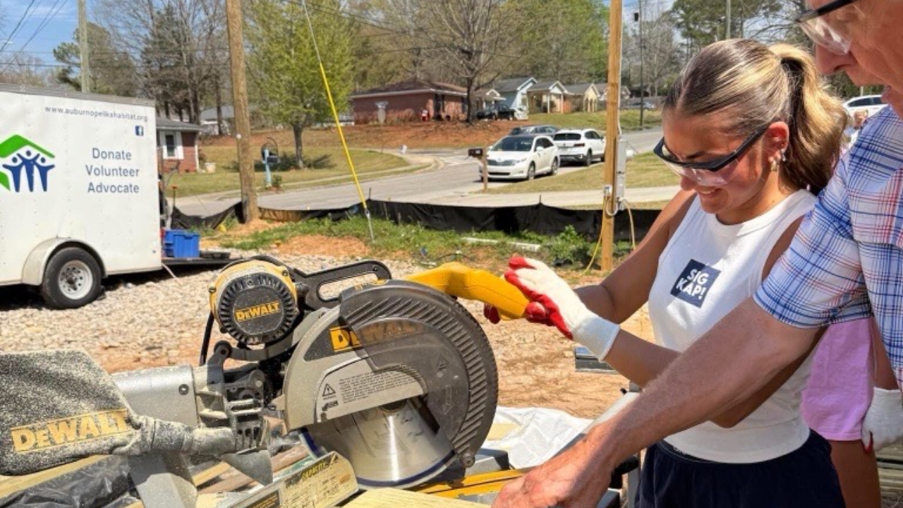 Woman using a miter saw on a Habitat for Humanity local project worksite.
