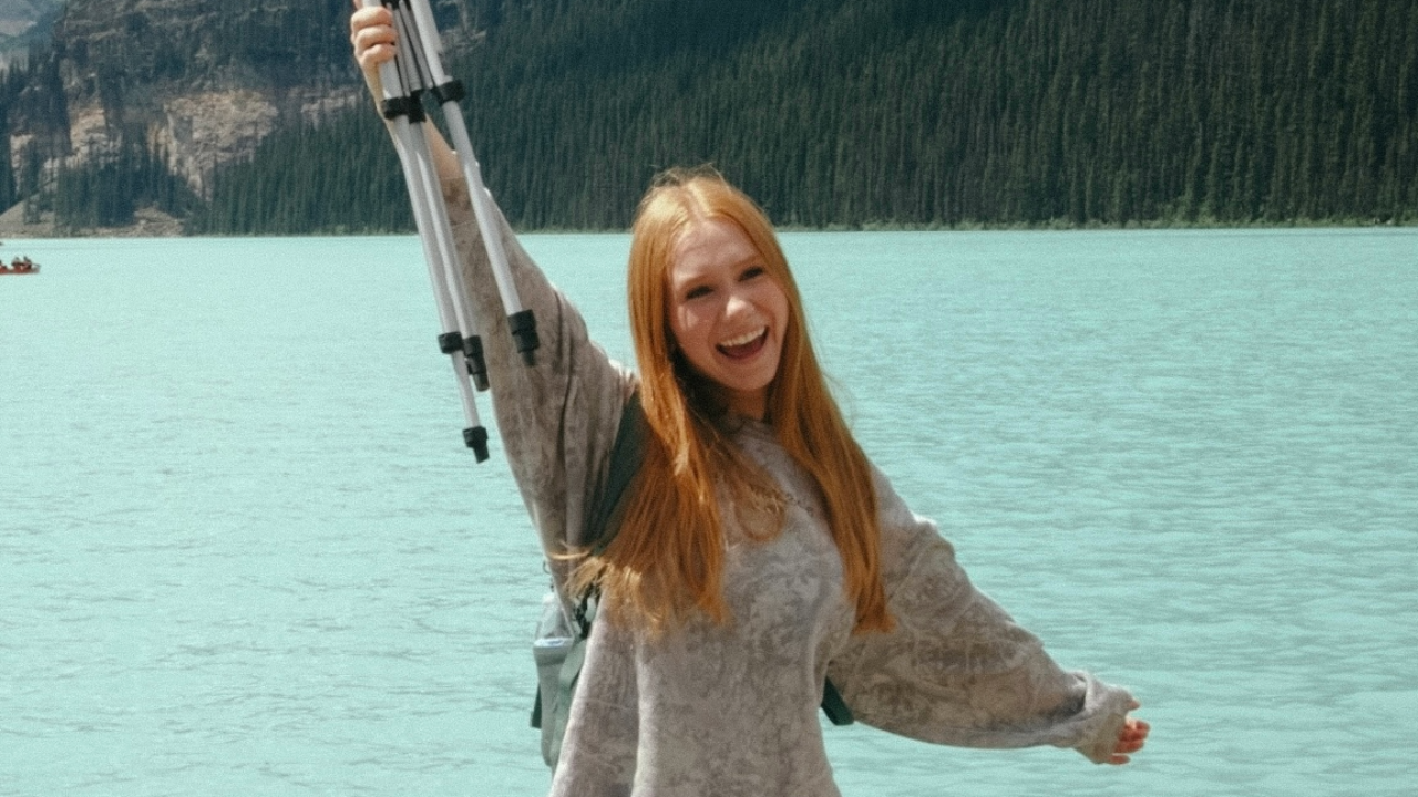 Girl with raised arms in front of blue water.