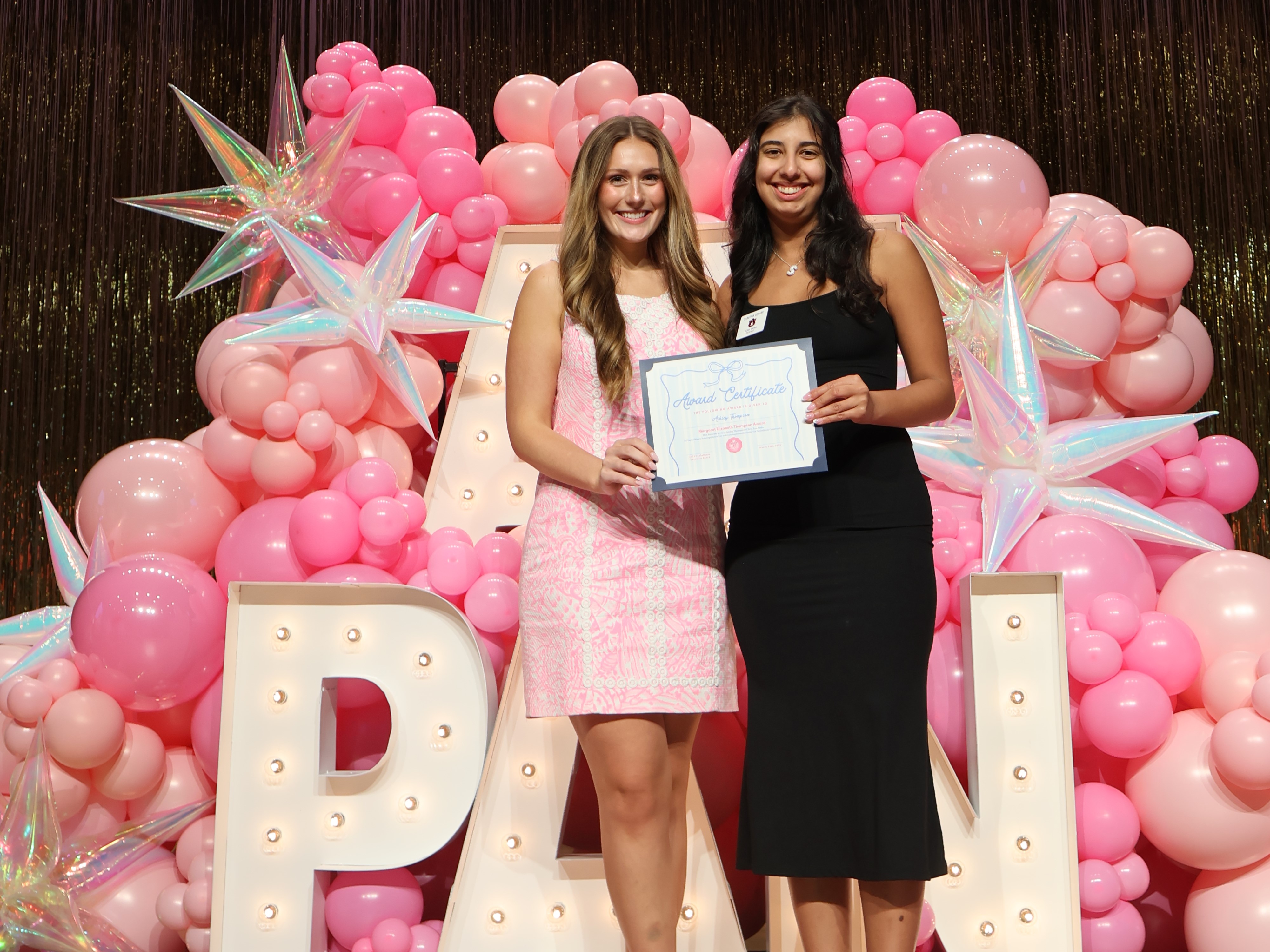 Two women holding a certificate in front of a balloon display.