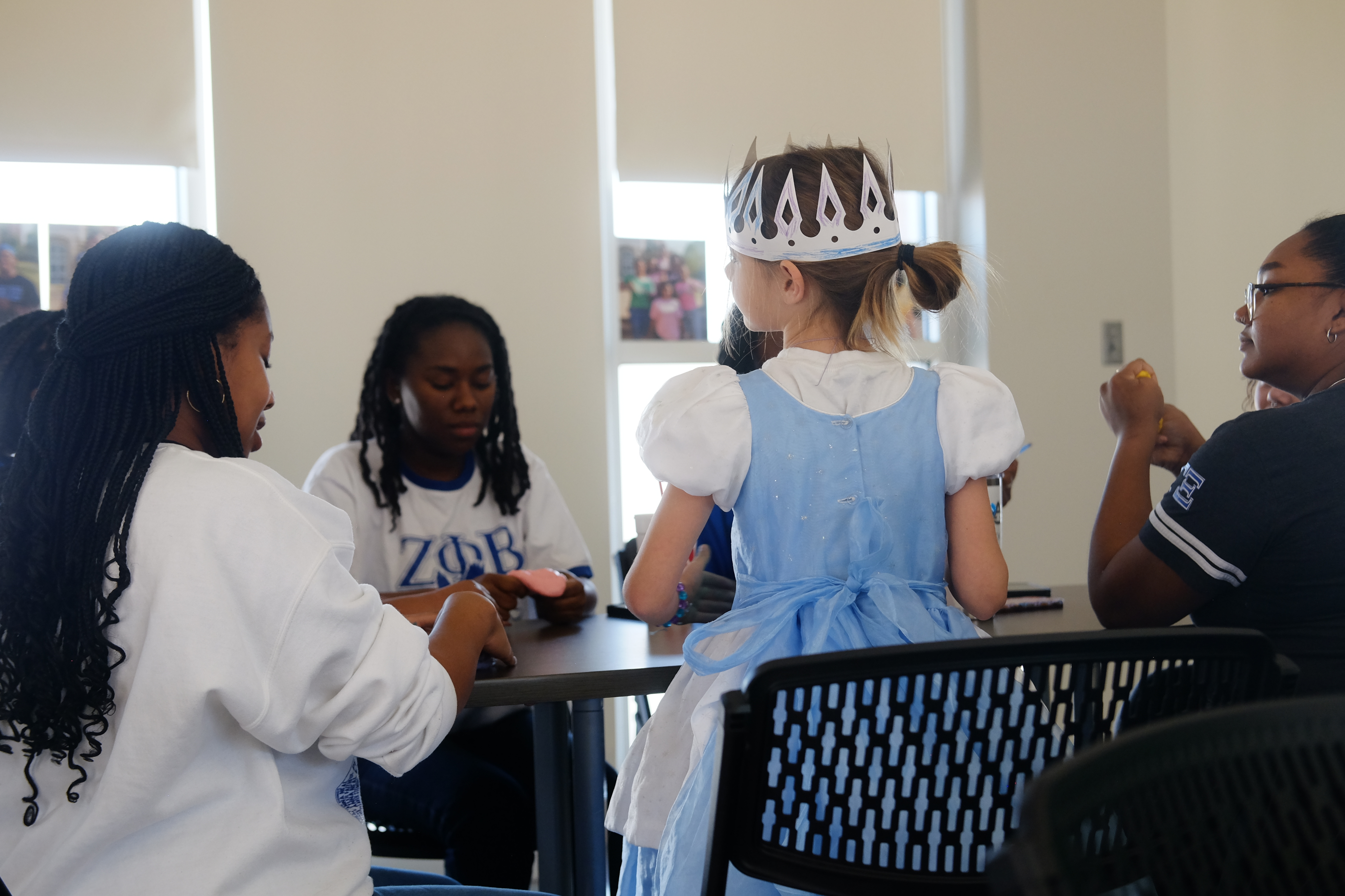 Young girl in a princess outfit sitting at a table with women.