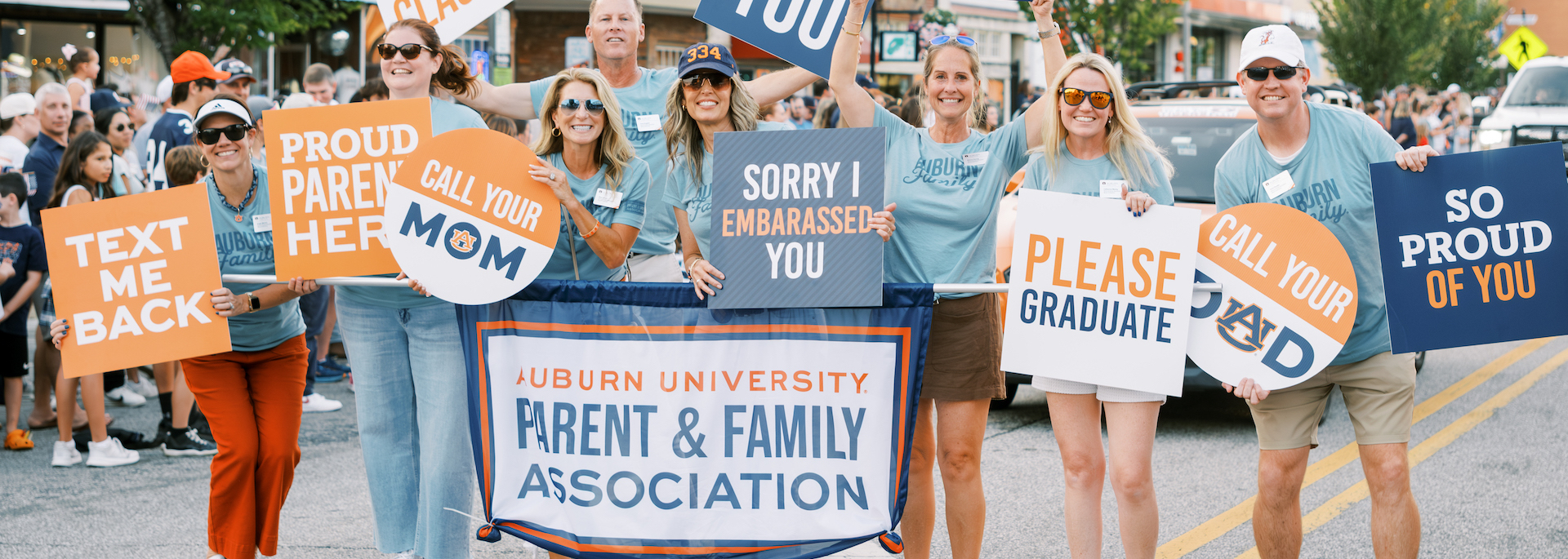 Parents and students holding various signs while walking in the 2025 Auburn Homecoming parade