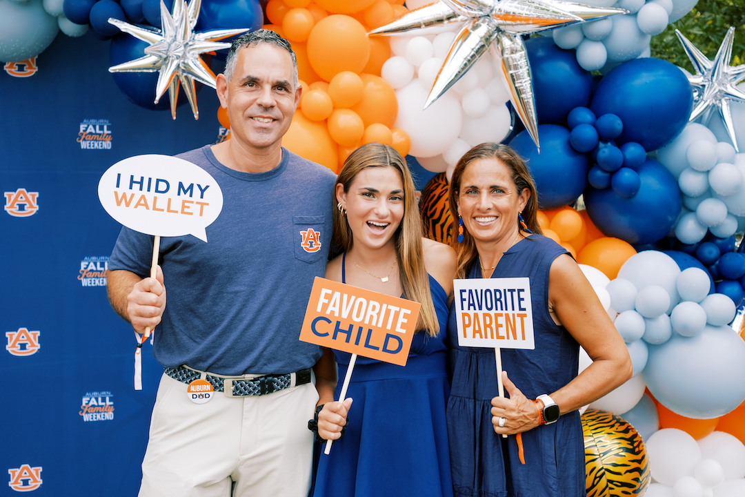 mom, dad, and daughter posing in front of a balloon backdrop with funny signs