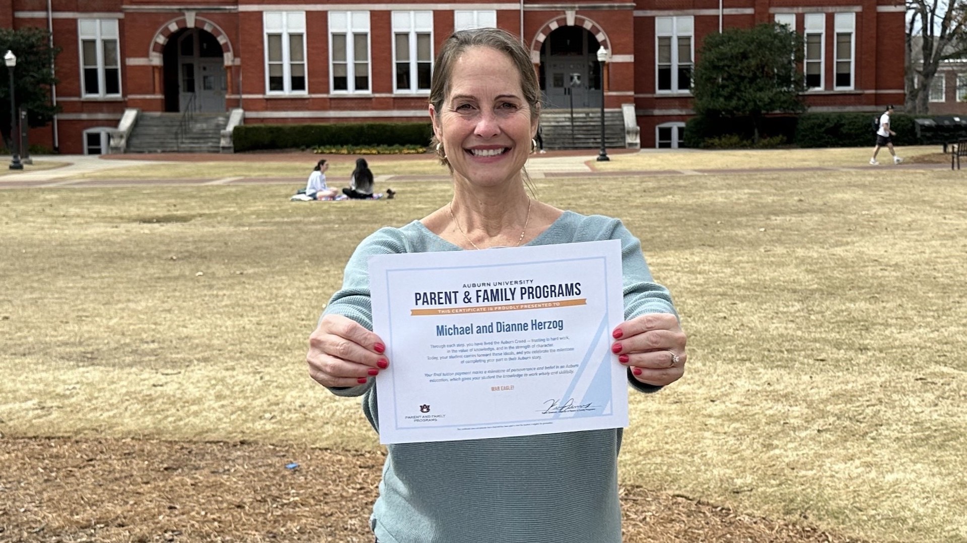 a mom holds her triumph over tuition certificate on Samford Lawn