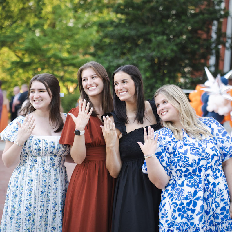four students in front of Samford hall showing off their Auburn rings