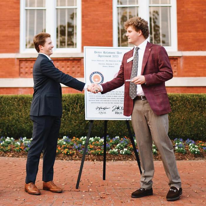 SGA presidents from Auburn University and University of Alabama shake hands in front of Samford Hall